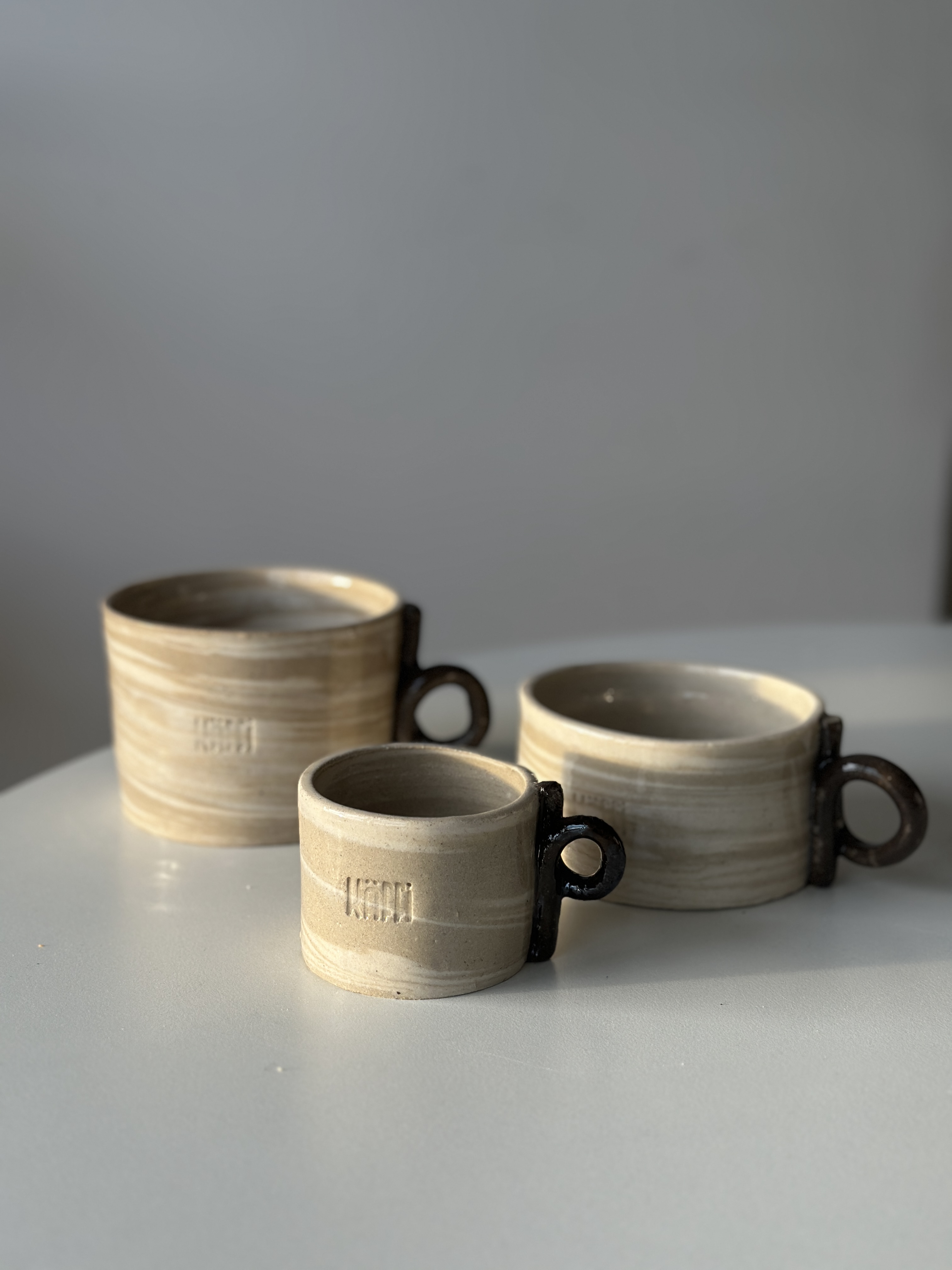Käffi finished pieces · three mugs with marbled bodies and dark glazed ring handles.