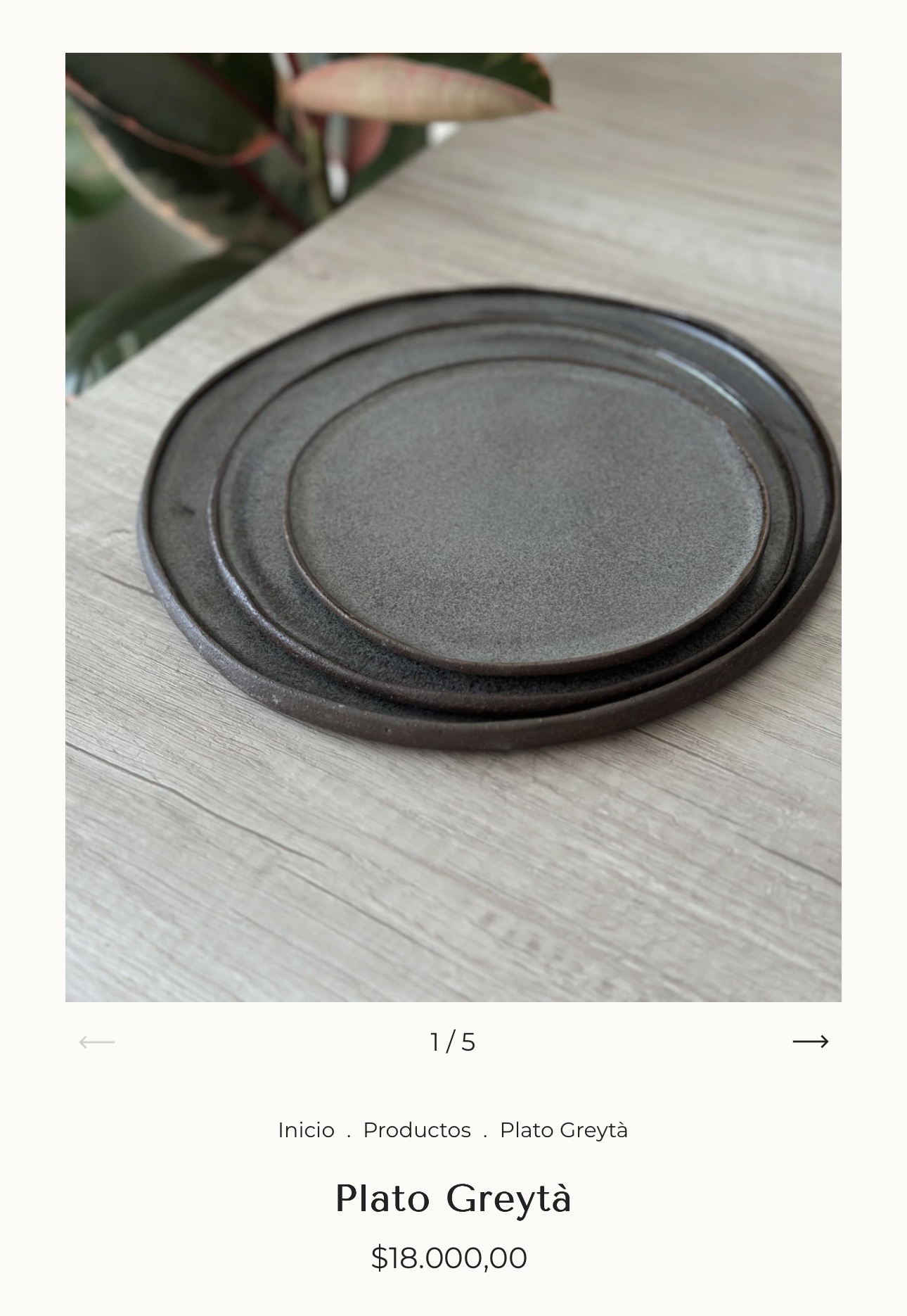 Plato Greytà · stacked stoneware plates with dark earthy glaze on a wood surface.