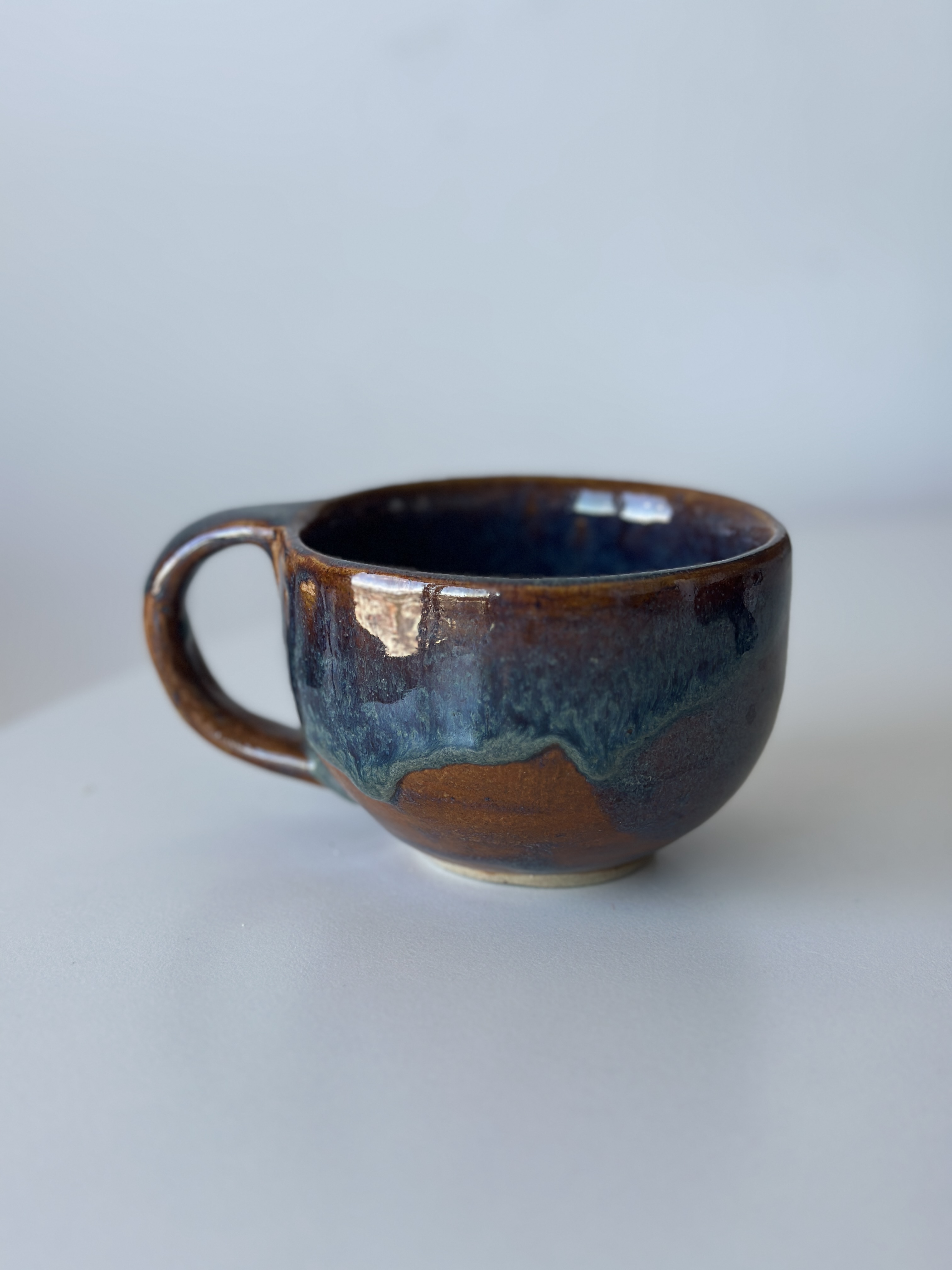 Taza Halo · cobalt drip glaze pooling over warm copper-rust body, soft daylight.