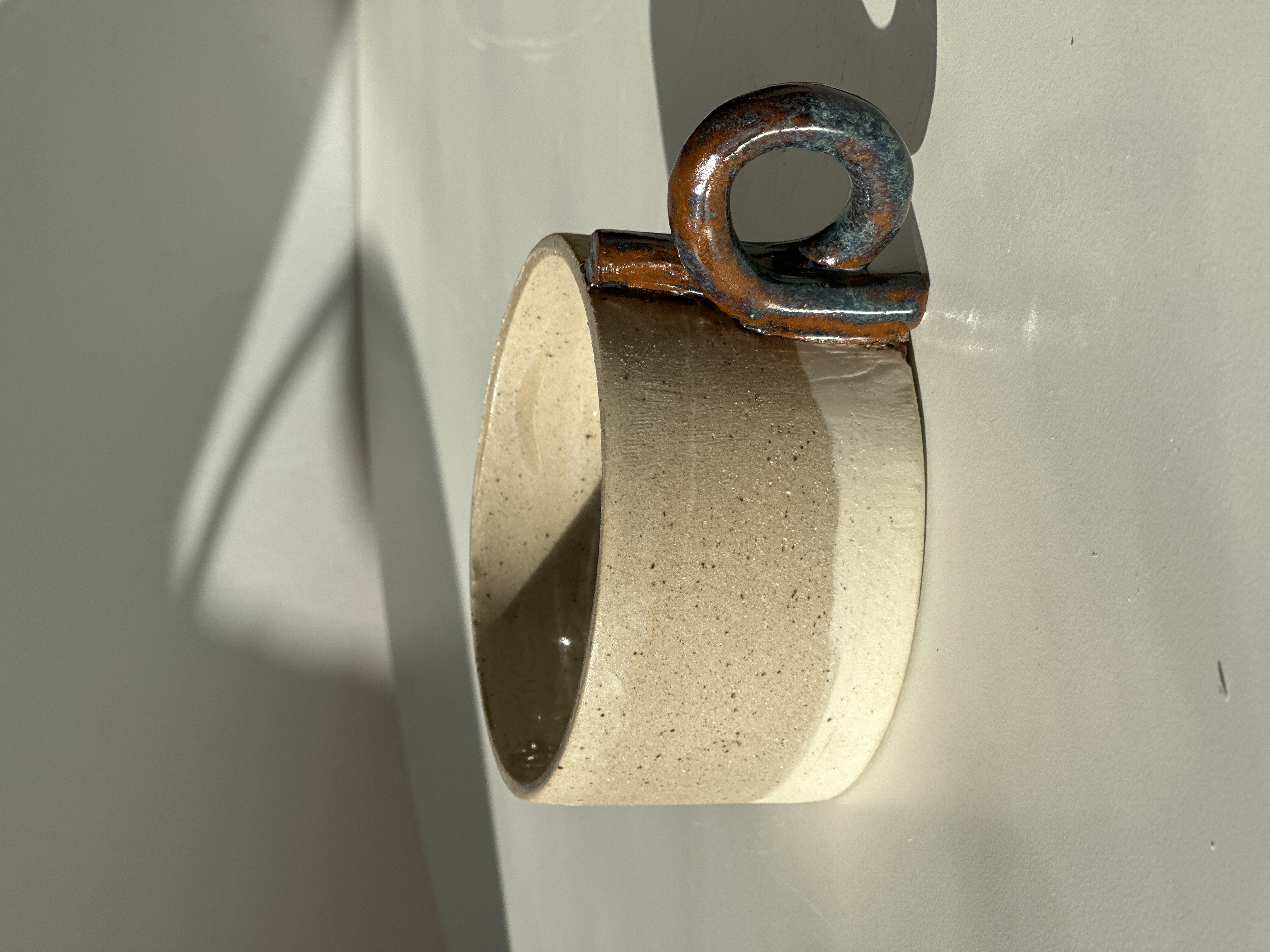 Taza Loop · raw stoneware cup with copper-iridescent ring handle in warm side light.
