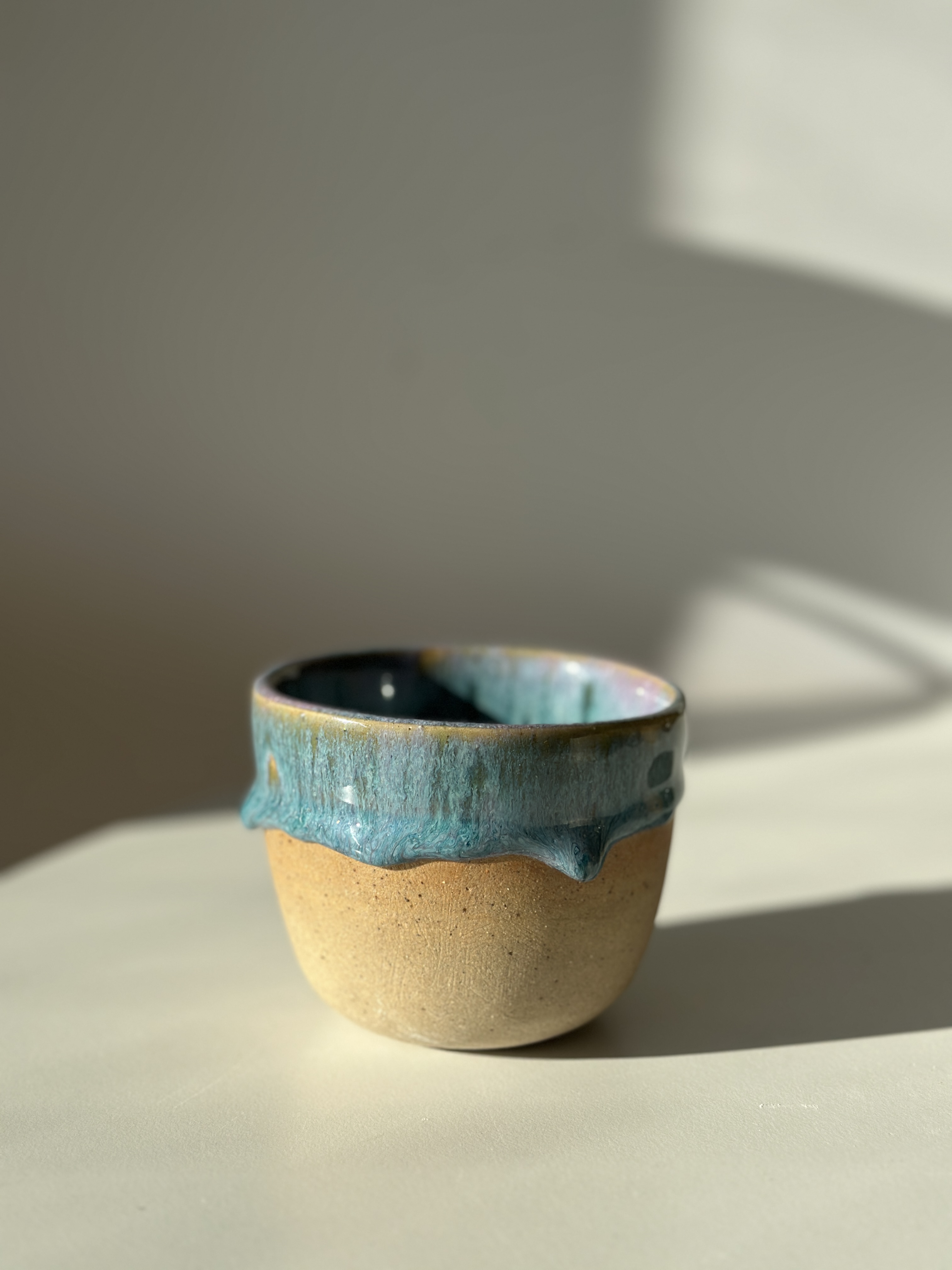 Taza Mar · raw stoneware base with dripping turquoise iridescent glaze, lit by warm side light.